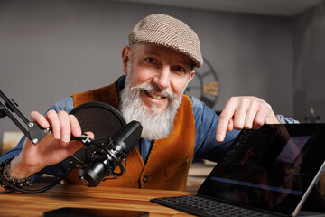 Studio podcast avec un micro et un ordinateur tablette et un homme souriant au look stylé et vintage avec une barbe hipster - 769783439