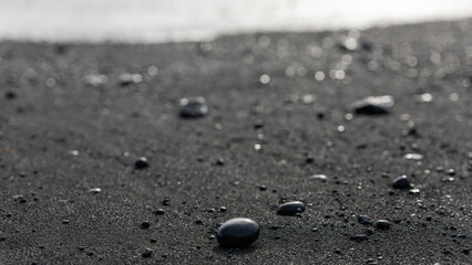 Fototapeta na wymiar Volcanic black rocks and sand on the black sand beach in Reynisfjara in Iceland on March 2024