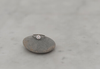 Antique platinum ring with single brilliant diamond on grey boulder on carrara marble surface. Selective focus