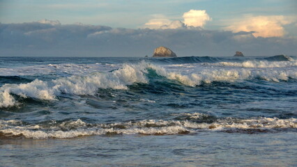 Waves breaking on the beach, with a small, rocky islet just off the coast, in Zipolite, Mexico