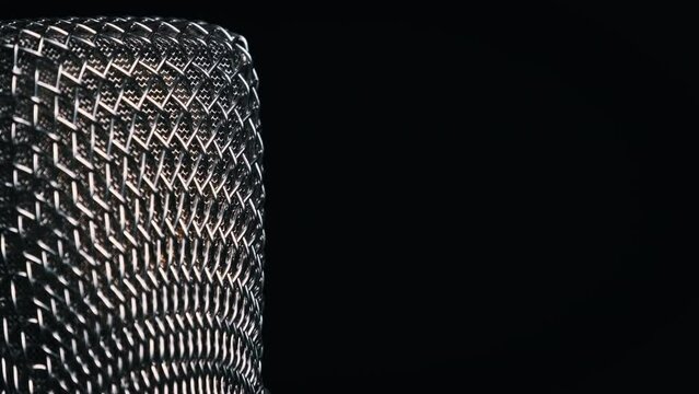 The studio condenser microphone rotates on a black background close-up. Chrome grid of mic surface spinning around. Concept recording studio, voice, podcast, audiobook. Copy space, place for text