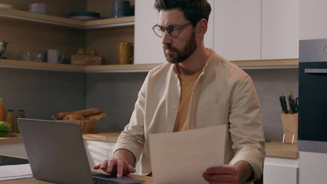 Caucasian man husband renter homeowner pay bills online on website app paperwork planning budget finances mortgage payments using laptop computer at kitchen freelancer working with documents at home