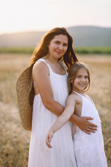 Happy mother in summer dress hugs her daughter on the field. Happy motherhood concept. Photoshooting mother and daughter. Summer season