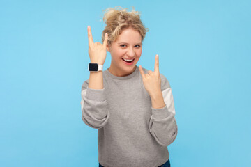 Portrait of cool smiling blonde woman showing rock and roll gesture having fun at rock concertor...