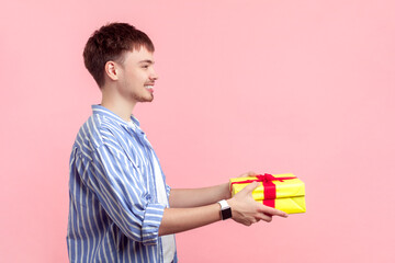 Side view portrait of smiling happy young man wearing shirt standing holding yellow present box...