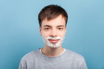 Portrait of smiling attractive man wearing gray jumper standing with face shaving foam doing...