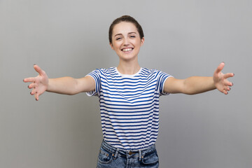 Come into my arms. Portrait of happy positive woman wearing striped T-shirt reaching out to camera,...
