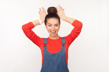 Portrait of funny positive woman with hair bun making bunny ears, having fun, demonstrates childish...