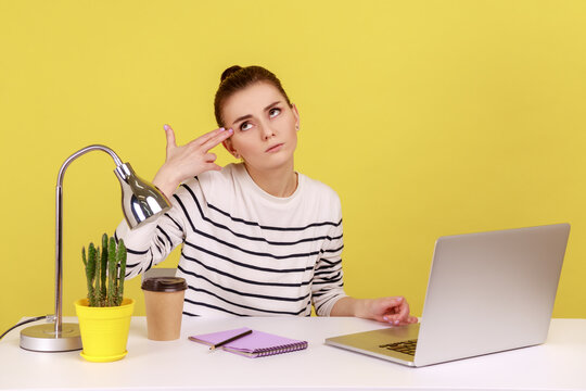 Depressed overworked woman office worker holding fingers near temple imitating gun shot, feeling stress and pressure because of work problems. Indoor studio studio shot isolated on yellow background.