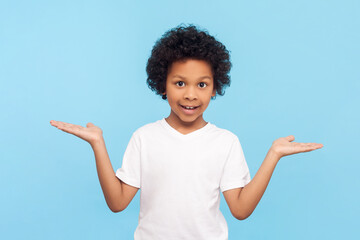 Portrait of cheerful joyful positive little boy with curly hair presenting copy space on his palms...