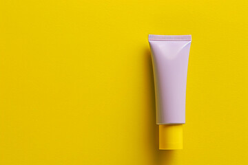 Modern cosmetic cream tube with a matte lavender finish against a bright yellow isolated solid...