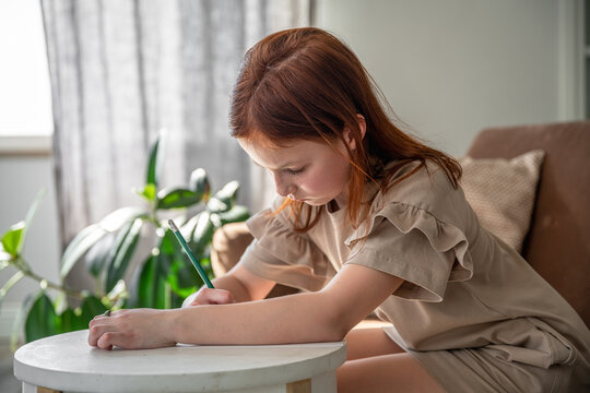 cute little preteen girl drawing with pen while sitting at desk at home, beautiful female child, small kid doing school homework