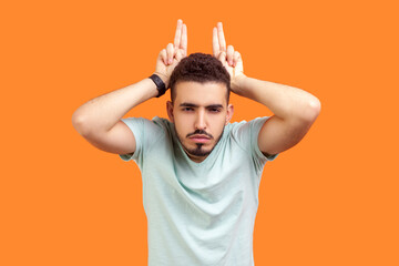 Portrait of angry young bearded man wearing T-shirt showing devil horns demonstrating arguing with...