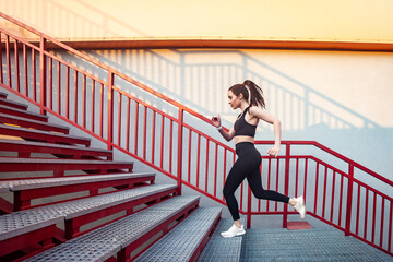 Full length portrait of slim athletic sporty woman wearing black sportswear doing physical exercising running on stairs training her body having cardio workout outdoor.