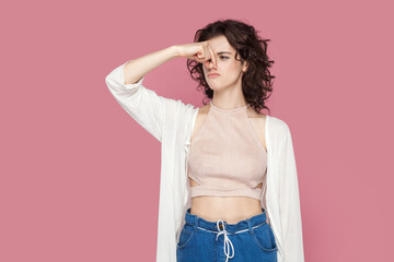 Portrait of beautiful woman with curly hair wearing casual style outfit pinching her nose, smelling bad smell, expressing disgust. Indoor studio shot isolated on pink background.