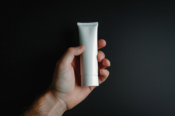 Hand gripping an empty white cosmetic cream tube against a matte black isolated solid background, highlighting elegance and premium skincare,