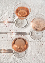 Rose wine in vintage glasses with blooming pink branches, flower petals, romantic mood, spring vibes. Eco linen background, natural spring light, romantic still life