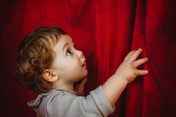 Foto op Aluminium child touching fabric of red curtain, looking up in awe © primopiano