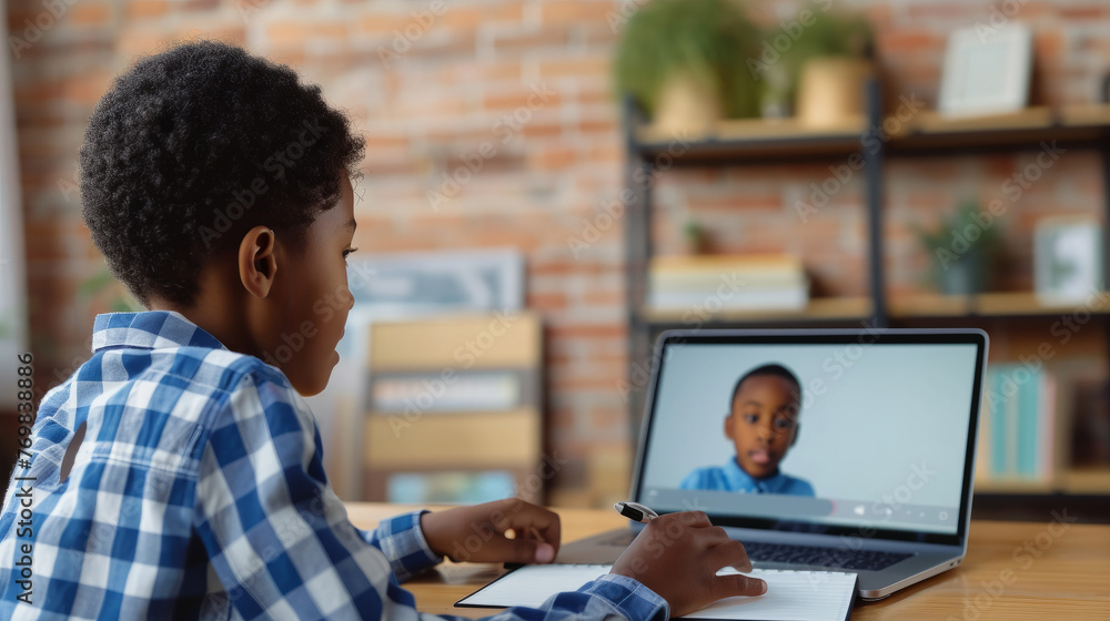Poster a young boy is sitting at a desk with a laptop open in front of him. he is writing in a notebook and