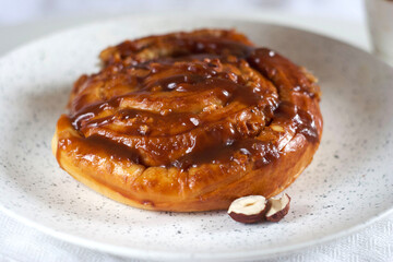 Bun with caramel and nuts in a plate on the table