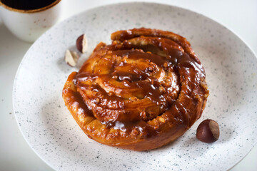 Bun with caramel and nuts in a plate on the table