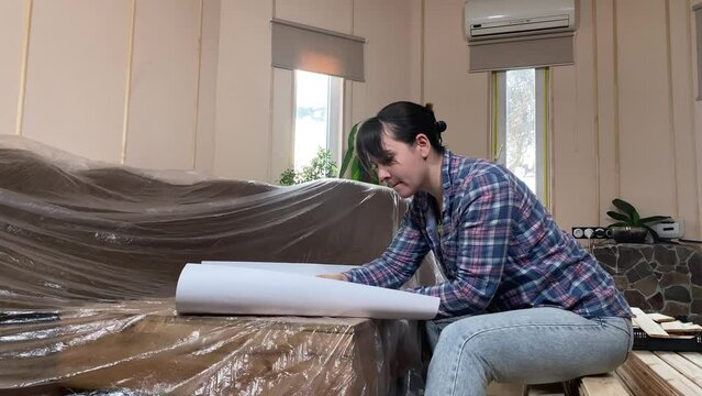 A beautiful young woman engages in home improvement, planning preparing for renovation on backdrop of construction materials indoors. Reconstruction, DIY concept. Handywoman makes remodeling plan
