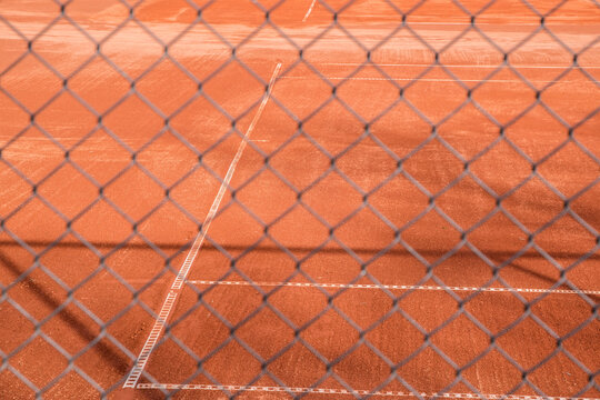 Red clay tennis court surface seen through chain link metal fence