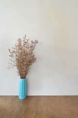 Dried flower in turquoise vase on wooden table over beige wall - 769851230