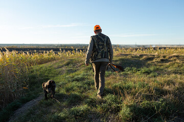 Mature man hunter with gun while walking on field.