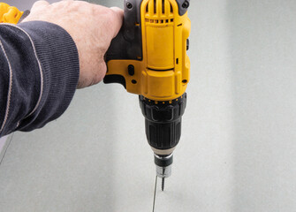 a worker's hand holding an electric drill with a drywall screw clutch setter ready to drive another...