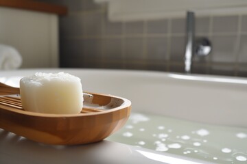 solid shampoo on a wooden soap dish beside a bathtub - 769863471