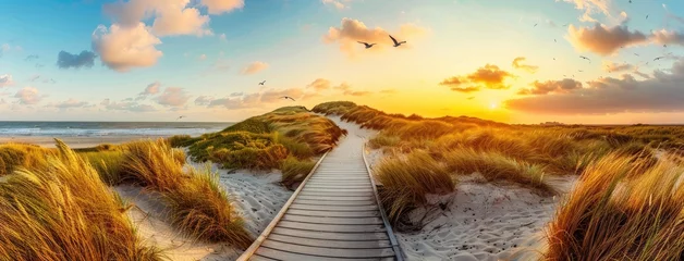  a wooden boardwalk leading to the sea at sunset, offering a mesmerizing panoramic view of dunes, grassland landscape, and seagulls soaring against a stunning sky. © lililia