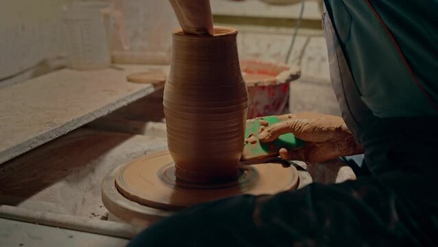 Potter shapes the clay jug with special tools when product rotates. Old man hobby in workshop. Professional masterclass of sculpting. Ukrainian traditional molding earthenware