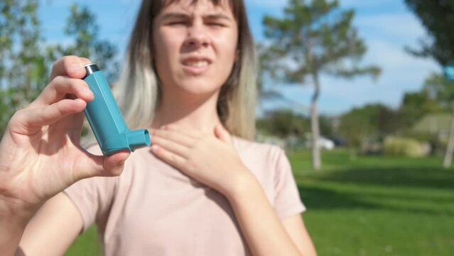 Teen with allergies troubles. A sad modern teen girl use her inhaler in the park because of allergy disease.
