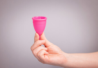A woman holds a menstrual cup in her hands. pink menstrual cup on a gray background. close-up of a...