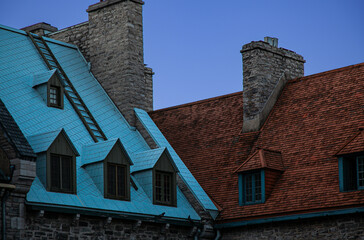 Colorful rooftops with dormer windows and stonework chimneys of residential buildings against a blue sky in historic Old Quebec in Quebec City, Canada