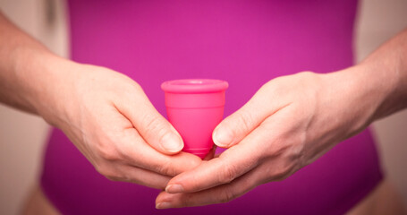 A woman holds a pink menstrual cup in her hands. Zero waste concept. Alternative feminine hygiene...