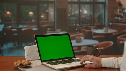 A man working on a laptop with green screen in evening cafe. Advertising area, workspace mock up.
