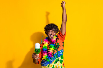 Photo of overjoyed man wear print shirt hold drink raising arm scream yeah celebrate vacation...