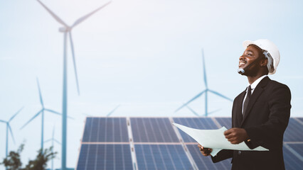 African engineer manager stand holding blueprint front solar photovoltaic and wind turbines...