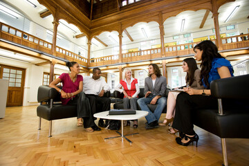 Open Meeting. A group of relaxed young professionals sitting to discuss a group project in their open plan atrium meeting space.