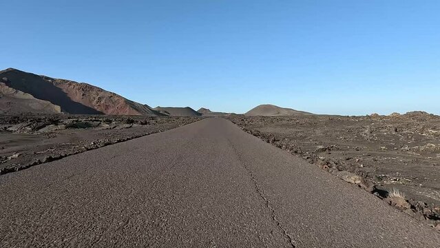 Vehicle view driving over Lanzarote Parque Nacional de Timanfaya national park showing the rough landscape left and right of the road of the volcanic rock and mountain in background 4k resolution