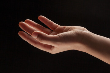 A boy's delicate left hand with palm facing up on a black background