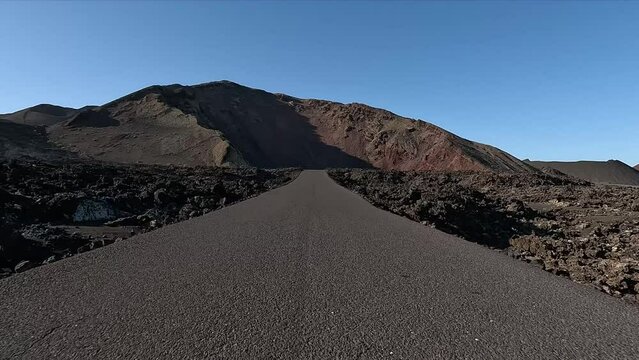 Vehicle hood view driving over Lanzarote Parque Nacional de Timanfaya national park showing the rough landscape left and right of the road of the volcanic rock and mountain in background 4k resolution