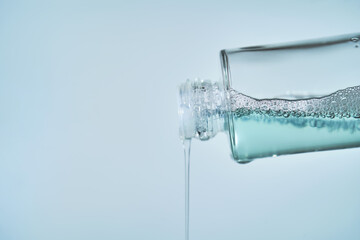 Cosmetic bottle from which serum is pouring on a blue background.