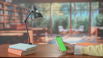 Mobile phone with green screen in hands of woman in background of library. Advertising area, workspace mock up.