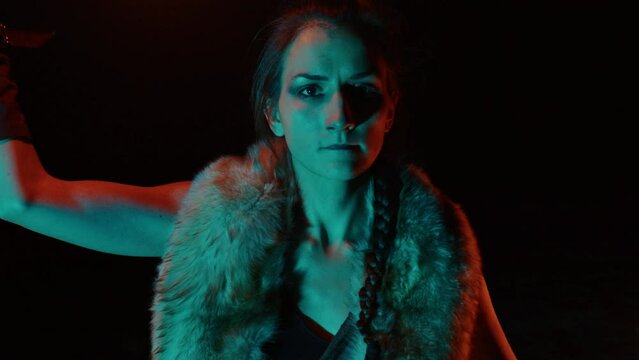 Mystical spectacular fire performance in night. Female artist in tribal costume twirls rod lit at ends in hands. Young attractive woman revolves flamy props outdoors. Close up portrait