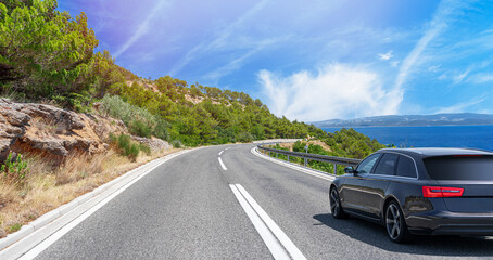 Black car drives along the sea coastline on a sunny summer day.