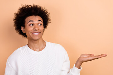 Photo of satisfied man wear white stylish jumper demonstrate news poster arm hold empty space isolated on beige color background