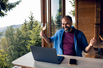 Man having a virtual toast during video call in a home with forest in the background